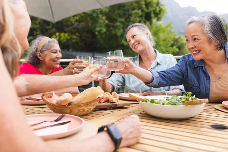 Four residents share an outdoor dining experience on a patio, toasting with drinks and enjoying a meal together.