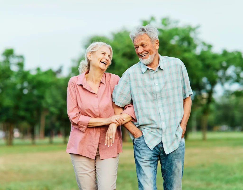 Two residents walk arm-in-arm, laughing joyfully in a grassy outdoor area.
