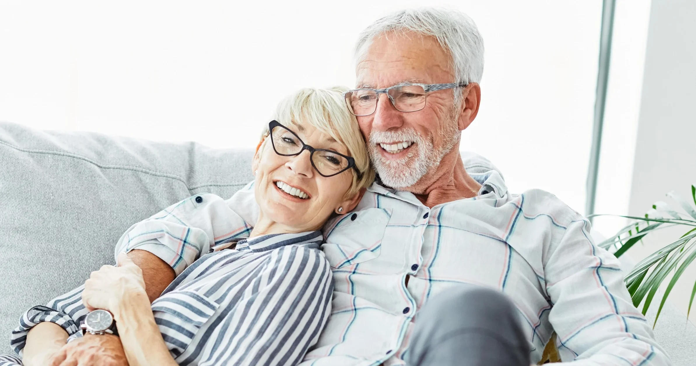 Two residents sitting closely and smiling together on a couch in a bright room with a plant nearby.